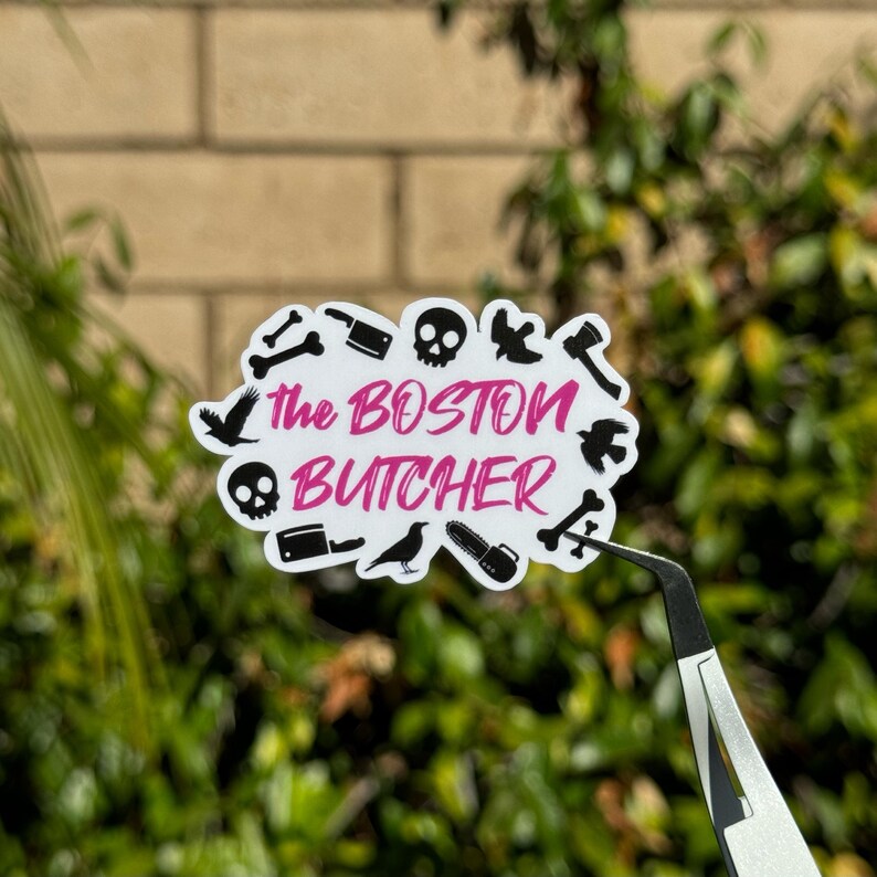 May include: White sticker with black and pink text that reads "The Boston Butcher" surrounded by black silhouettes of various objects, including a skull, a crow, a bone, a knife, and a chainsaw.