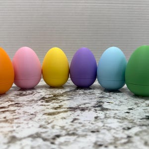 May include: Six colorful Easter eggs in a rainbow pattern. The eggs are orange, pink, yellow, purple, light blue, and green.
