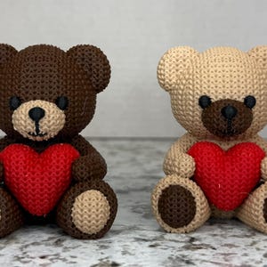 May include: Two knitted teddy bears holding red hearts. The bears are brown and beige.