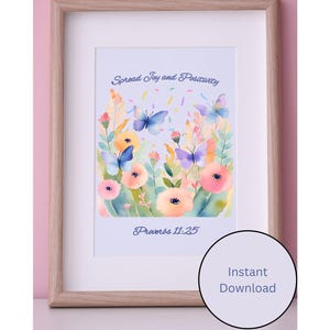 Könnte beinhalten: Ein gerahmter Aquarelldruck mit einem Blumen- und Schmetterlingsdesign. Das Kunstwerk enthält den Text "Spread Joy and Positivity" und "Proverbs 11:25". Der Rahmen ist hellbraun mit einem weißen Passepartout, der Hintergrund ist rosa.