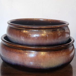 May include: Two brown ceramic bowls stacked on top of each other. The bowls have a glossy finish with a gradient of colors, transitioning from dark brown to lighter shades. The bowls are round with a wide rim.