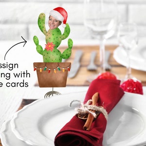 Könnte beinhalten: Ein skurriler weihnachtlicher Tischkartenhalter mit einem Kaktus, der einen Weihnachtsmannhut trägt. Der Kaktus steht in einem braunen Topf, der mit Lichterketten verziert ist. Der Text "Assign seating with place cards" ist ebenfalls sichtbar.