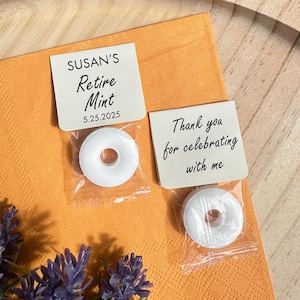 May include: Two small white favor bags with white round mints inside. One bag has a tag that says "SUSAN'S Retire Mint 5.25.2025". The other bag has a tag that says "Thank you for celebrating with me".
