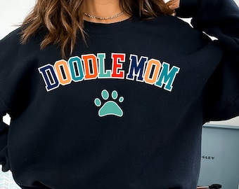 May include: Black sweatshirt with the text "Doodle Mom" in rainbow colours and a teal paw print.