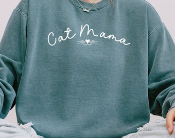 May include: A teal blue sweatshirt with the text "Cat Mama" in white cursive lettering with a small heart and cat whiskers underneath.
