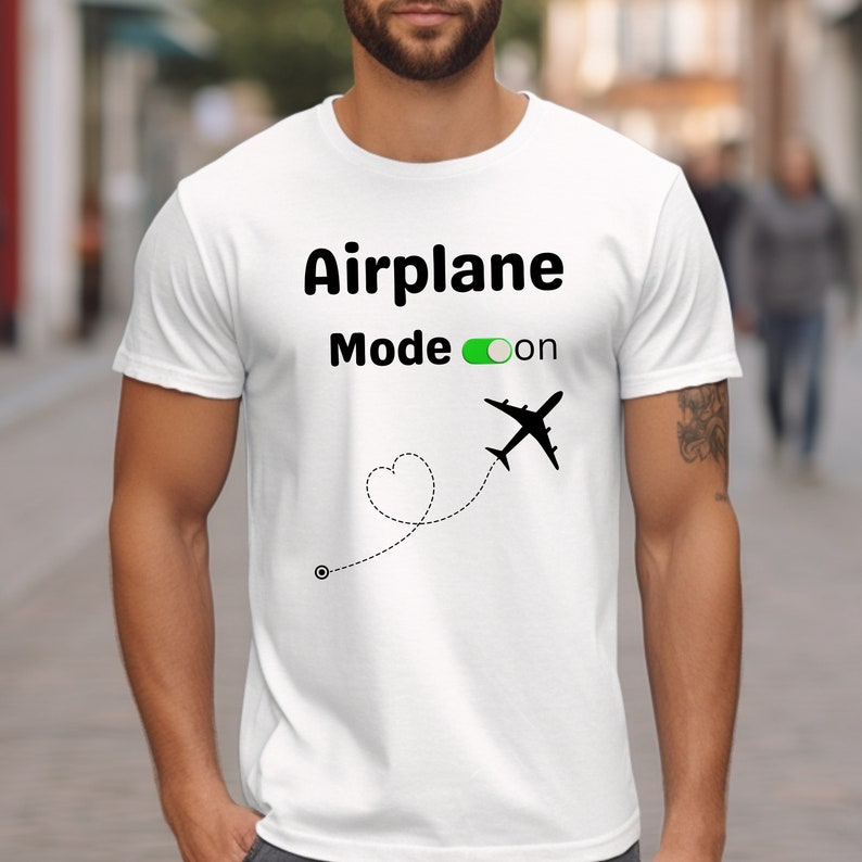 May include: White t-shirt with black text that reads "Airplane Mode on" with a green toggle switch and a black airplane with a dotted line and heart shape trailing behind it.