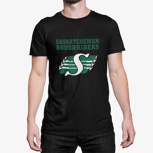 May include: Black t-shirt featuring a green and white Saskatchewan Roughriders logo. The logo depicts a stylised "S" with lightning bolts and wheat stalks.