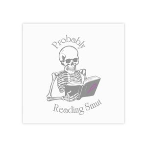 May include: Square sticker with a skeleton reading a book. The text "Probably Reading Smut" is arched above the skeleton and below the book. The book has a pink cover with a lipstick mark.