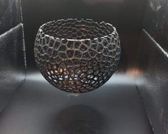 May include: A black, 3D printed, spherical bowl with a geometric, openwork design. The bowl is suspended in mid-air, casting a shadow on the black surface below.