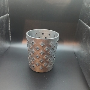 Op de afbeelding: Een zwarte, 3D-geprinte, cilindrische plantenpot met een geometrisch patroon en drainagegaten.