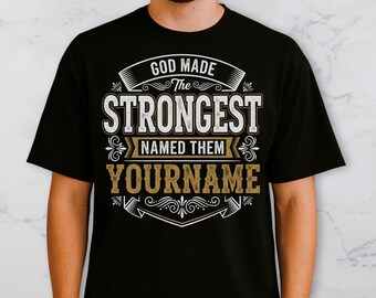 May include: Black t-shirt with the text "GOD MADE THE STRONGEST NAMED THEM YOURNAME" in white and gold lettering. The design features decorative flourishes and a banner-style layout, suitable for personalized gifts.