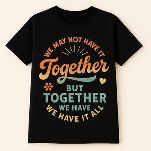 May include: Black t-shirt with the text "WE MAY NOT HAVE IT TOGETHER BUT TOGETHER WE HAVE IT ALL" in orange, teal, and white. The design includes a flower and heart graphic.