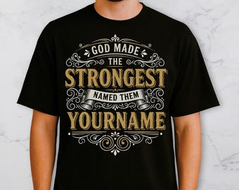 May include: Black t-shirt with a gold and white design. The text reads "GOD MADE THE STRONGEST NAMED THEM YOURNAME" in a decorative font. The shirt is a crew neck style.