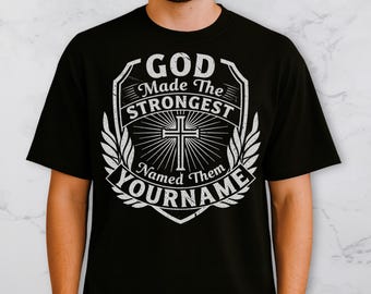 May include: Black t-shirt with a white graphic design. The design features the text "GOD Made The STRONGEST Named Them YOURNAME" around a cross and sunburst design. The shirt is a crew neck.