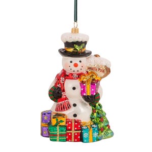 Op de afbeelding: Een kerstversiering in de vorm van een sneeuwpop met een zwarte hoge hoed, een rode sjaal en een bord met de tekst "Noordpool". De sneeuwpop heeft een stapel kleurrijke cadeaus en een kleine kerstboom.