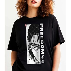 May include: Black t-shirt with a black and white illustration of a character's face and the word "FREEDOM" in white vertical text. The design includes Japanese characters. The shirt is short-sleeved.