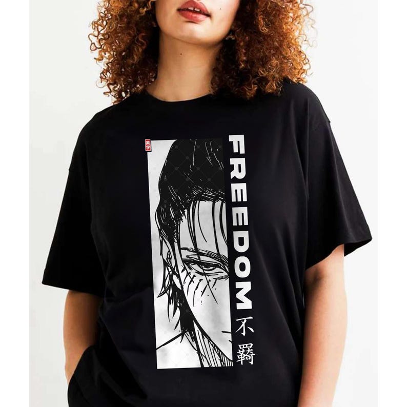 May include: Black t-shirt with a black and white illustration of a character's face and the word "FREEDOM" in white vertical text. The design includes Japanese characters. The shirt is short-sleeved.