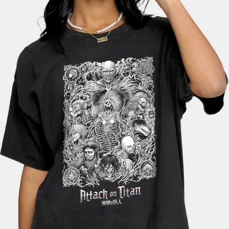 May include: Black t-shirt with a white graphic print of characters from the anime Attack on Titan. The graphic features a detailed illustration of the characters in a stylized design. The text "Attack on Titan" and "進撃の巨人" are printed below the graphic.