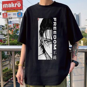 May include: Black t-shirt with a black and white illustration of a character's face and the word "FREEDOM" in white vertically. The shirt also has text in a foreign language.
