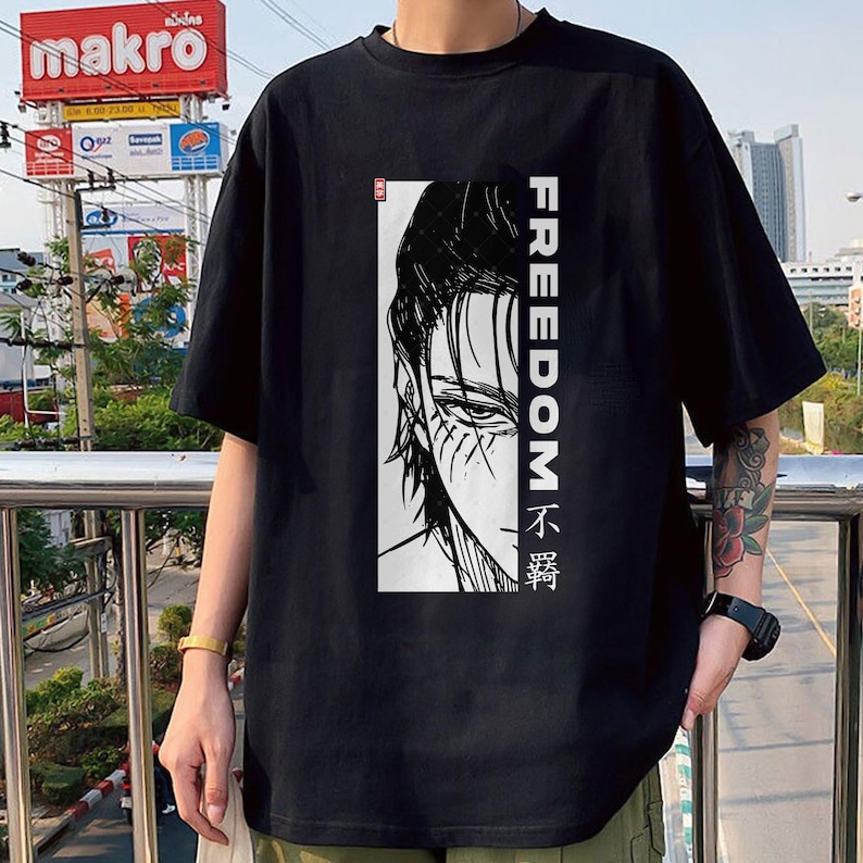 May include: Black t-shirt with a black and white illustration of a character's face and the word "FREEDOM" in white vertically. The shirt also has text in a foreign language.