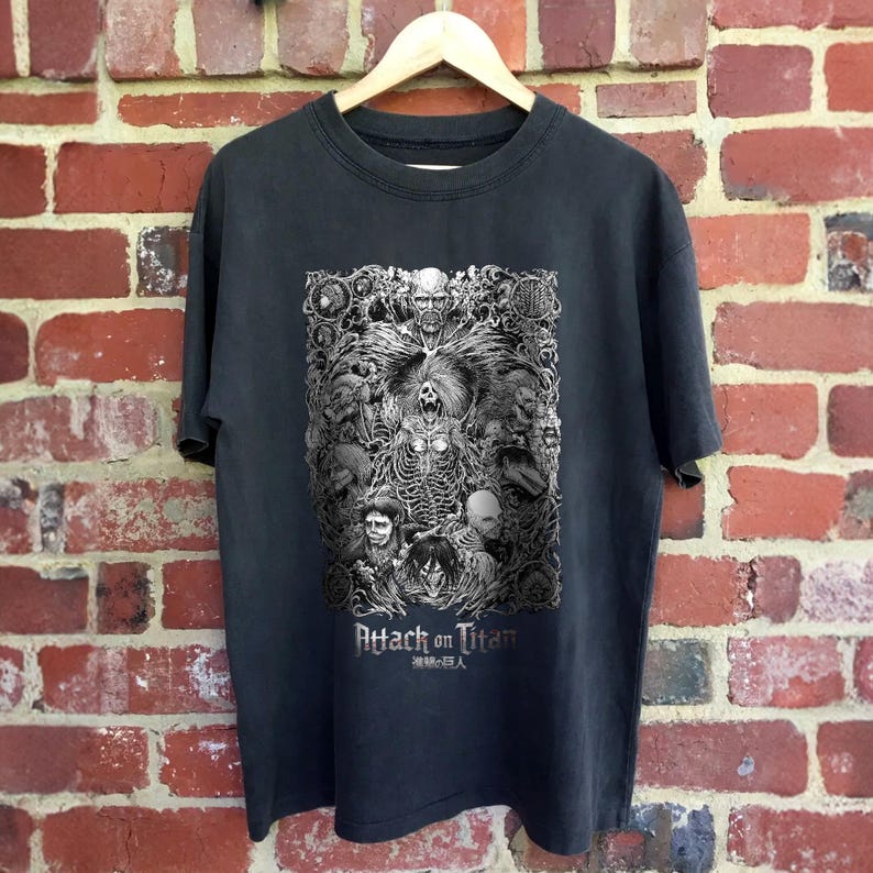May include: Black t-shirt with a white graphic print of characters from the anime Attack on Titan. The text "Attack on Titan" and "進撃の巨人" are printed below the graphic.