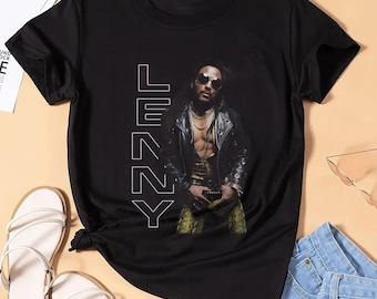Puede incluir: Camiseta negra con un retrato de una persona con gafas de sol y una chaqueta de cuero. La palabra "LENNY" está impresa verticalmente en blanco. La camiseta se combina con sandalias blancas y pantalones cortos vaqueros.