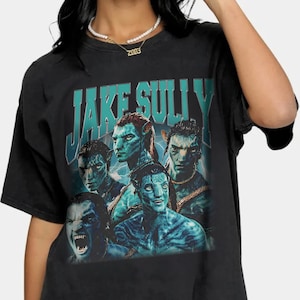 May include: Black t-shirt with a vintage-style graphic of Jake Sully and other Na'vi characters from the movie Avatar. The text "JAKE SULLY" is printed in a bold, blue font.