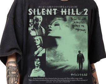 May include: Black t-shirt featuring a graphic from Silent Hill 2. The design includes images of characters, the game's title, and text in English and Japanese. The shirt's design has a distressed, vintage look.