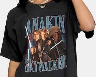 Puede incluir: Camiseta negra con un gráfico de estilo vintage de Anakin Skywalker y otros personajes de Star Wars. El texto "Anakin Skywalker" está impreso en letras azules y blancas.