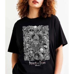 May include: Black t-shirt with a white graphic print of characters from the anime Attack on Titan. The graphic features a detailed illustration of the characters in a stylized design. The text "Attack on Titan" and "進撃の巨人" are printed below the graphic.