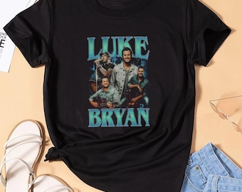 Puede incluir: Camiseta negra con un gráfico degradado azul de Luke Bryan y el texto "LUKE BRYAN". El diseño incluye un collage de imágenes del artista. La camiseta se combina con sandalias blancas y pantalones cortos vaqueros azules.