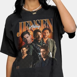 May include: Black t-shirt featuring a vintage-style graphic of Jensen Ackles. The design includes multiple images of the actor with the name "Jensen Ackles" in an orange and blue font. The shirt has a classic crew neck.