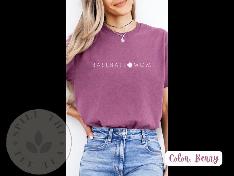 May include: A woman wearing a purple t-shirt with the text "BASEBALL MOM" and a baseball graphic. She is wearing blue jeans.