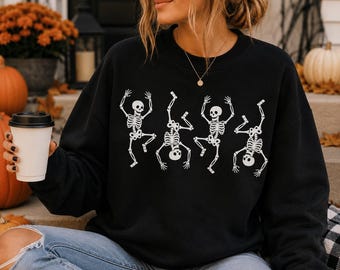May include: A black long-sleeve crewneck sweatshirt featuring a white graphic print of four skeletons in various dancing poses across the chest. The sweatshirt has a ribbed collar, cuffs, and hem, providing a standard fit for casual wear.