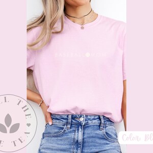 May include: A pink t-shirt with the text "Baseball Mom" in white lettering. The shirt is being worn by a person with long blonde hair. The person is wearing blue jeans.