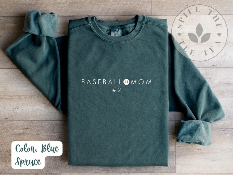May include: A dark green sweatshirt with the text "BASEBALL MOM #2" in white. The sweatshirt features a baseball graphic and is made from a soft, comfortable fabric.