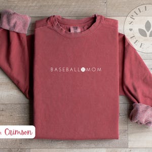 May include: Crimson red long-sleeved sweatshirt with the text "BASEBALL MOM" and a baseball graphic.