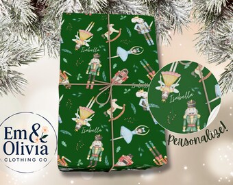 May include: A wrapped present with a green background featuring a repeating pattern of nutcrackers, ballerinas, and rocking horses. The name "Isabella" is written on the wrapping. The gift is tied with twine.