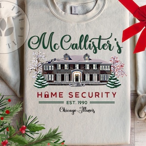 Puede incluir: Una sudadera beige de cuello redondo con un gr&aacute;fico de una casa grande en invierno con &aacute;rboles nevados. El texto dice "McCallister's HOME SECURITY EST. 1990 Chicago, Illinois" en letras verdes, rojas y negras con un icono de candado en la palabra home.