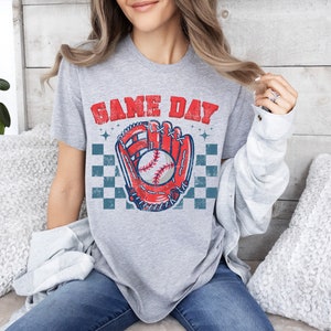 Pu&ograve; includere: Maglietta grigia con una grafica di guanto da baseball e palla in stile vintage. Il testo "GAME DAY" &egrave; stampato in un font usurato sopra la grafica.