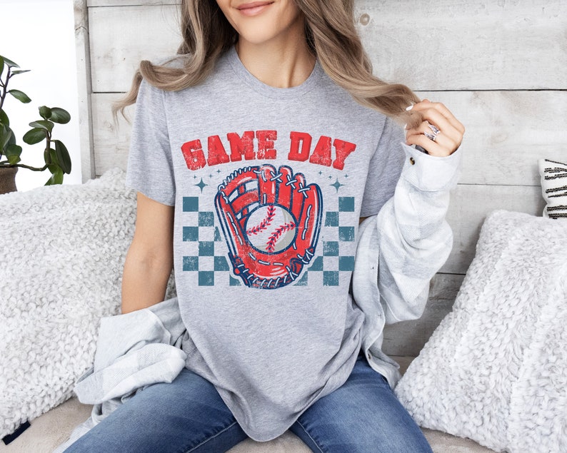 Pu&ograve; includere: Maglietta grigia con una grafica di guanto da baseball e palla in stile vintage. Il testo "GAME DAY" &egrave; stampato in un font usurato sopra la grafica.
