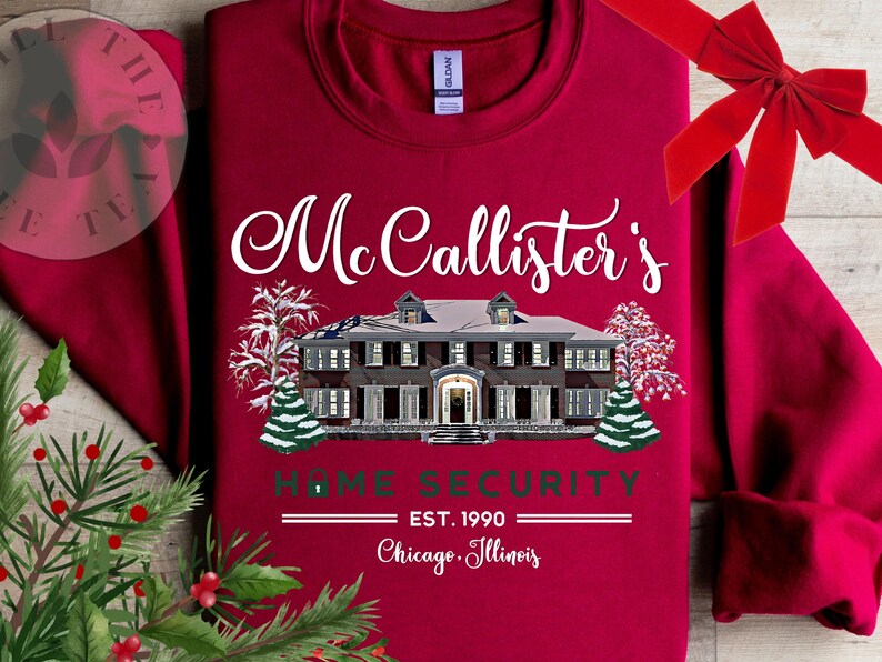 Puede incluir: Una sudadera de cuello redondo color rojo oscuro con el gr&aacute;fico de una casa grande cubierta de nieve. El texto dice McCallister's HOME SECURITY EST. 1990 Chicago, Illinois. El dise&ntilde;o incluye &aacute;rboles nevados y un icono de candado.