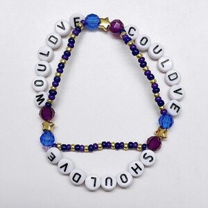Puede incluir: Un brazalete de cuentas con cuentas blancas que deletrean "Would've Should've Could've" y cuentas azules y moradas con estrellas doradas.