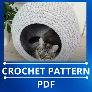 May include: Crochet pattern PDF for a gray cat bed. The bed is shaped like a sphere with a large opening for the cat to enter. A gray tabby cat is resting inside the bed.
