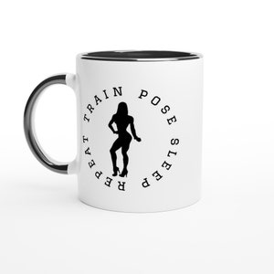 Könnte beinhalten: Weiße Keramiktasse mit schwarzem Rand. Die Tasse zeigt eine schwarze Silhouette einer Frau, die posiert, mit dem Text "Repeat Train Pose Sleep" um sie herum.