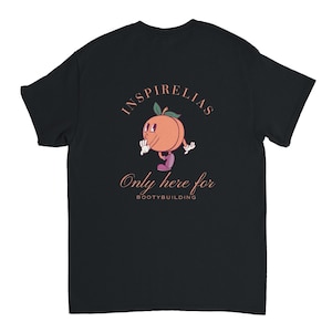 Könnte beinhalten: Schwarzes T-Shirt mit einer Cartoon-Pfirsichfigur. Der Pfirsich ist orange mit einem grünen Blatt und trägt lila Schuhe. Der Text lautet "INSPIRELIAS" oben und "Only here for BOOTYBUILDING" darunter.