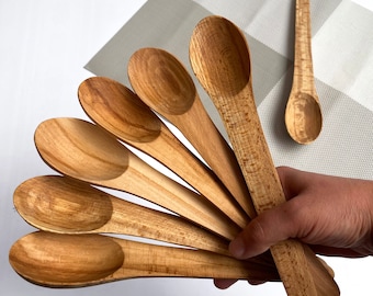 May include: A set of seven wooden spoons, all with a natural wood finish. The spoons are arranged in a fan shape, with the handles overlapping. The spoons are all the same size and shape, and they have a smooth, rounded bowl.