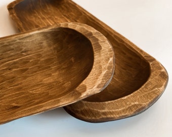 May include: Two wooden bread bowls, one nested inside the other. The bowls are a dark brown color and have a rustic, handmade appearance.