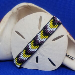May include: A beaded bracelet with a black, white, yellow, and purple geometric pattern.