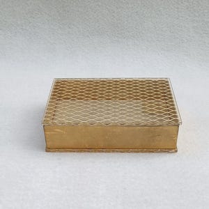 May include: A rectangular, gold-colored box with a lattice top. The box has a simple design with a clear, transparent lid and a gold-colored base. The lattice top is made of a fine, diamond-shaped mesh.